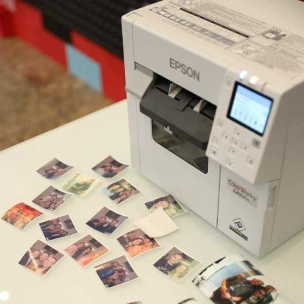 Ein Epson-Drucker druckt kleine Fotoaufkleber für eine photo mosaic wall bei einem Event in Berlin. Auf dem Tisch vor dem Drucker liegen zahlreiche frisch gedruckte Fotos, die später auf die Mosaikwand geklebt werden