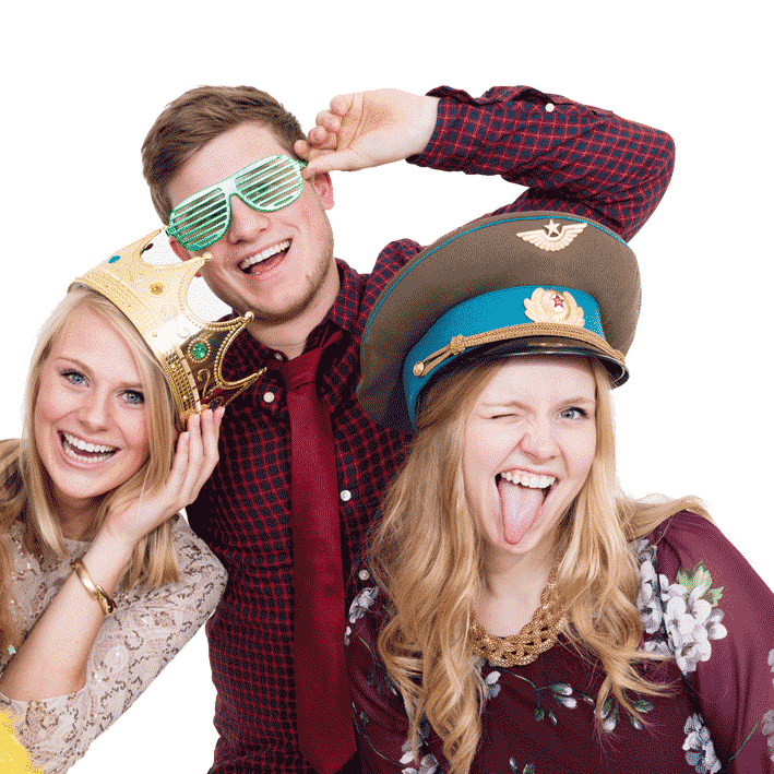 Drei fröhliche junge Erwachsene nutzen Accessoires aus einer 'Fotobox mieten' bei einer Party. Die Frau links trägt eine goldene Krone und lächelt, der Mann in der Mitte trägt grüne Streifen-Sonnenbrillen und zeigt das Victory-Zeichen, während die Frau rechts einen militärischen Hut trägt und frech die Zunge rausstreckt. Sie stehen vor einem einfarbigen grünen Hintergrund.