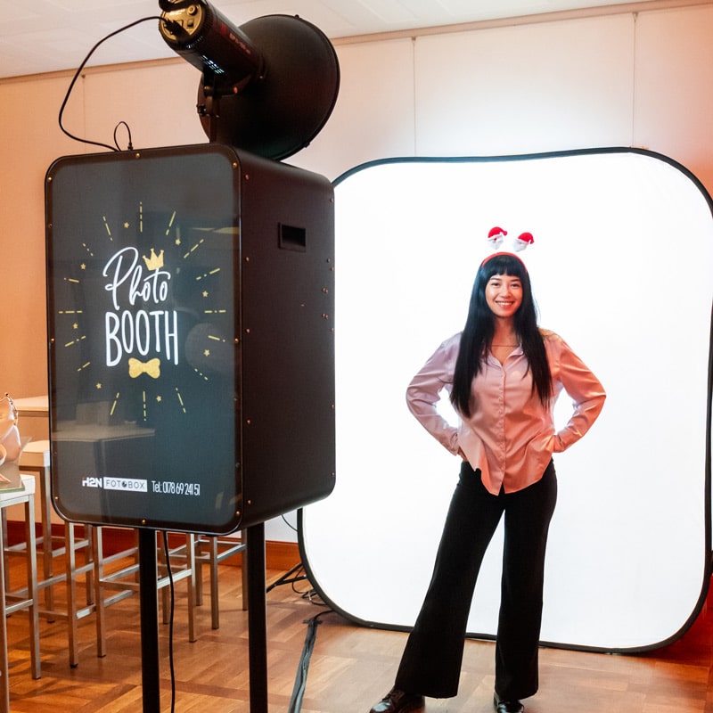 Eine Mitarbeiterin posiert fröhlich vor einer Fotobox mit der Aufschrift "Photo Booth" bei einem Event in Frankfurt.