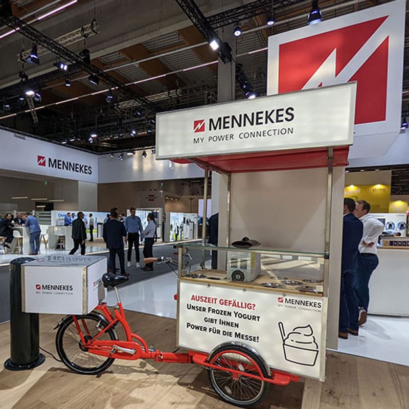 Eisfahrrad Messe mit gebrandeter Softeis-Station auf einem Messestand für Besucher und Kunden.