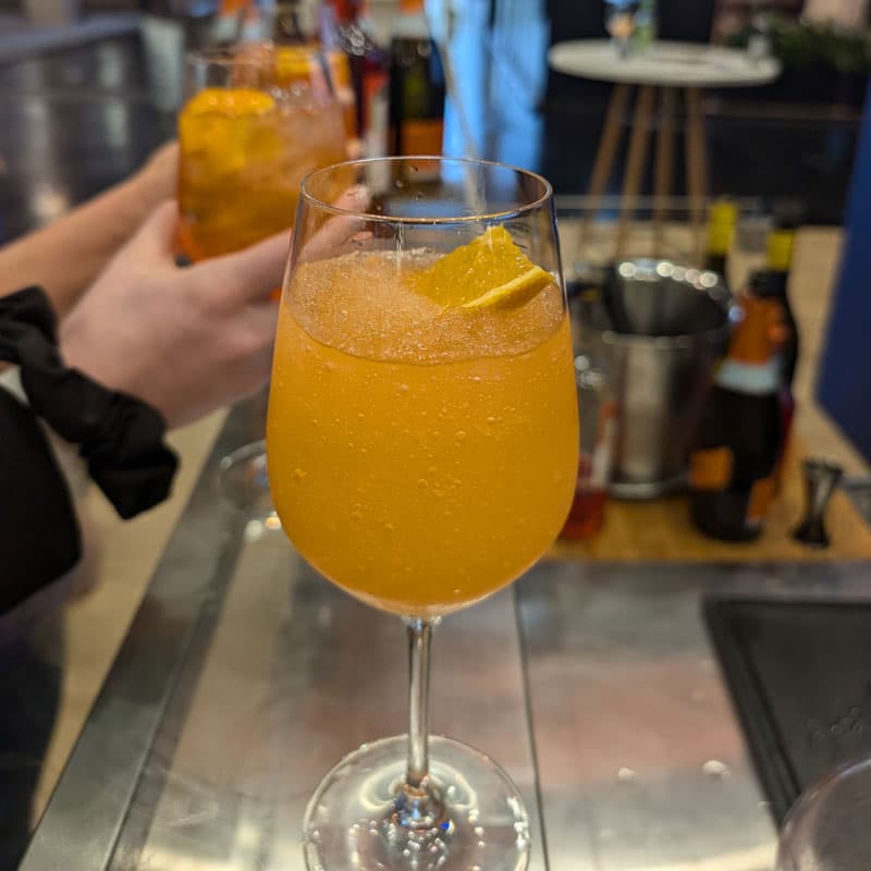 Aperol Spritz im Weinglas mit Orangenscheibe auf einer stilvollen Eventbar.