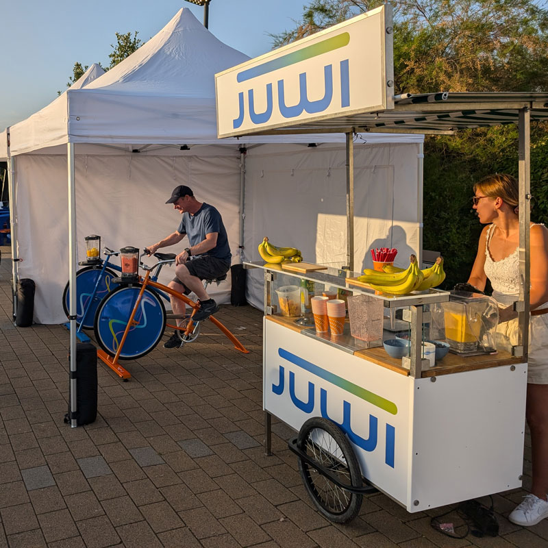 Besucher mixt einen Smoothie auf einem Fahrrad neben einer mobilen Getränkestation.